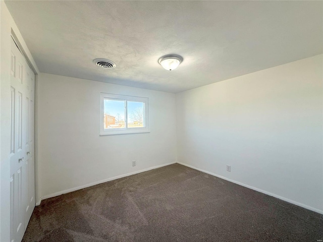 spare room featuring visible vents, dark carpet, and baseboards