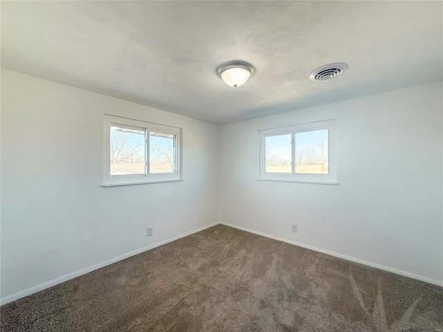 empty room featuring baseboards, visible vents, and dark colored carpet