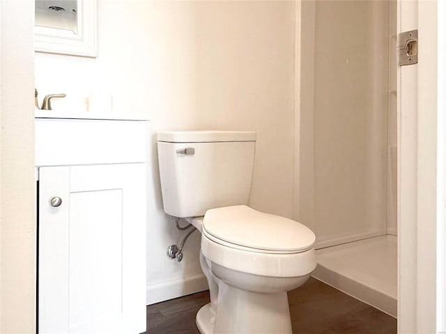 bathroom featuring baseboards, walk in shower, toilet, wood finished floors, and vanity