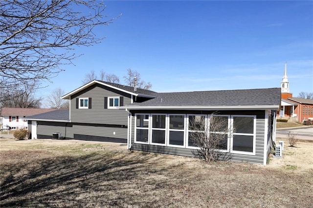 back of property with cooling unit, roof with shingles, and a sunroom