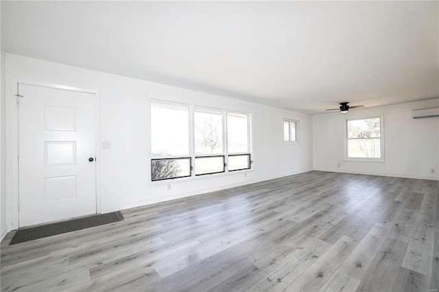 unfurnished room with baseboards, an AC wall unit, light wood-style flooring, and a ceiling fan