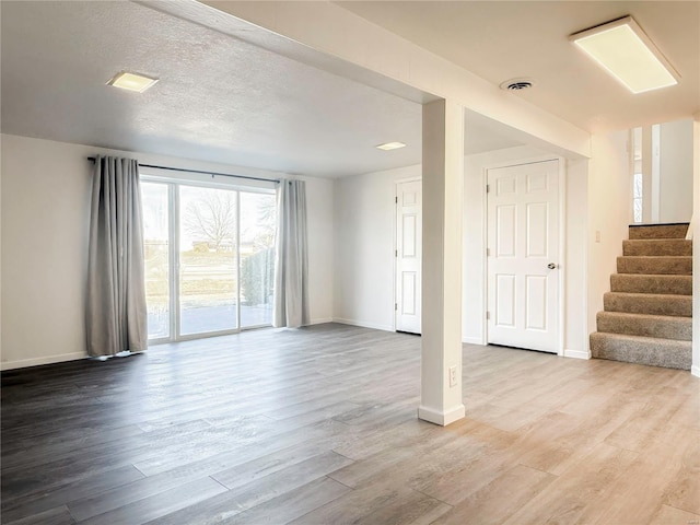 unfurnished living room featuring stairway, baseboards, visible vents, and wood finished floors