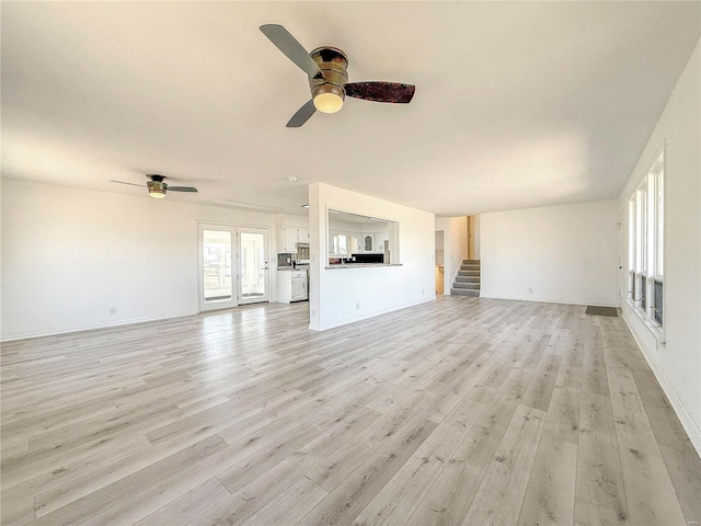 unfurnished living room with stairway, a ceiling fan, light wood-type flooring, and baseboards