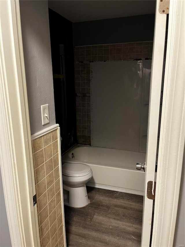 bathroom with wainscoting, toilet, wood finished floors, tub / shower combination, and tile walls