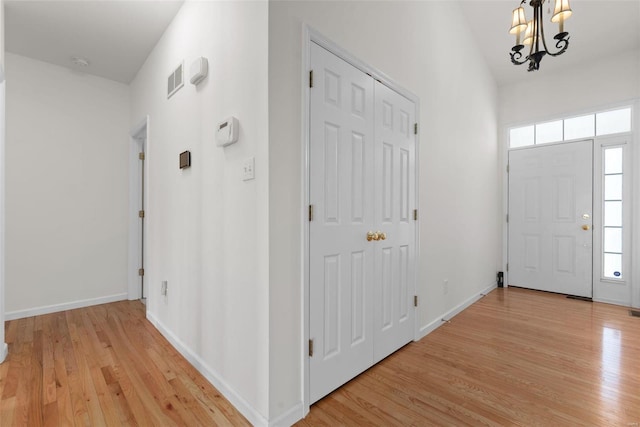 foyer featuring baseboards, light wood finished floors, visible vents, and a notable chandelier