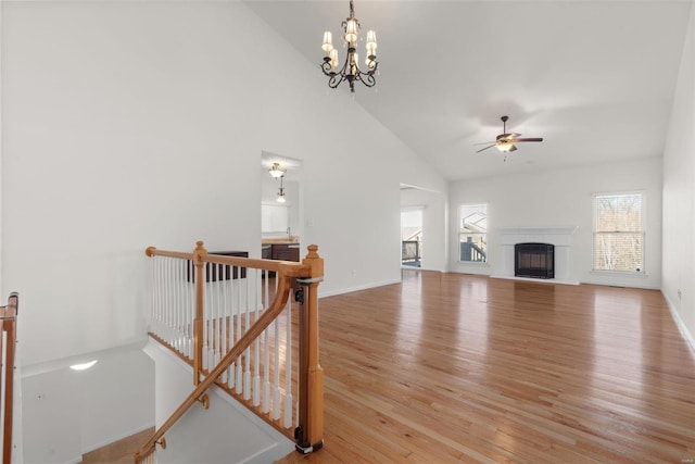 living room with a fireplace with raised hearth, high vaulted ceiling, wood finished floors, and baseboards