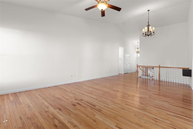 unfurnished room with high vaulted ceiling, light wood-style flooring, baseboards, and ceiling fan with notable chandelier