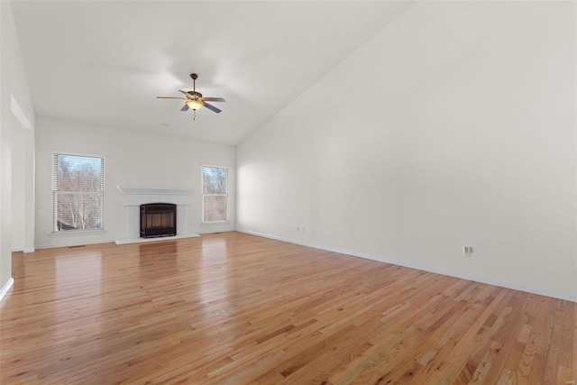 unfurnished living room with baseboards, a fireplace with raised hearth, a ceiling fan, light wood-style floors, and high vaulted ceiling