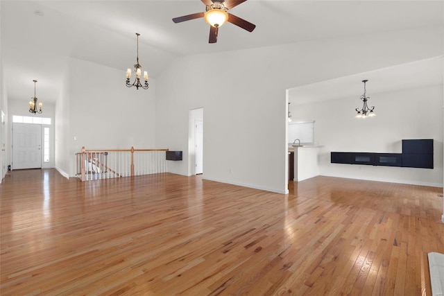 unfurnished living room with light wood-style floors, high vaulted ceiling, baseboards, and ceiling fan with notable chandelier