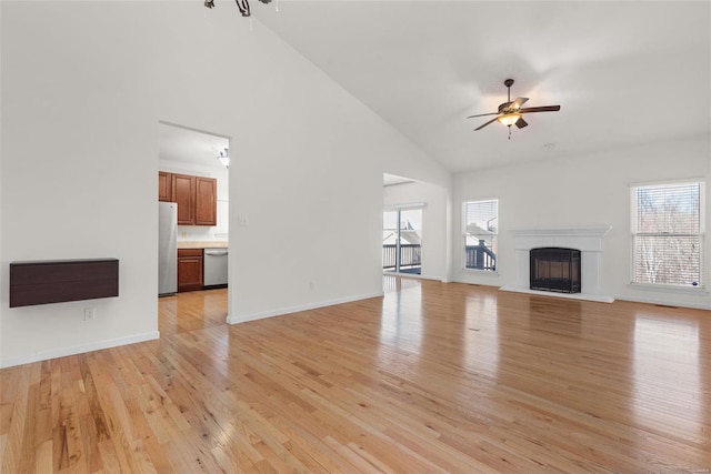 unfurnished living room featuring ceiling fan, plenty of natural light, a fireplace with raised hearth, and light wood finished floors