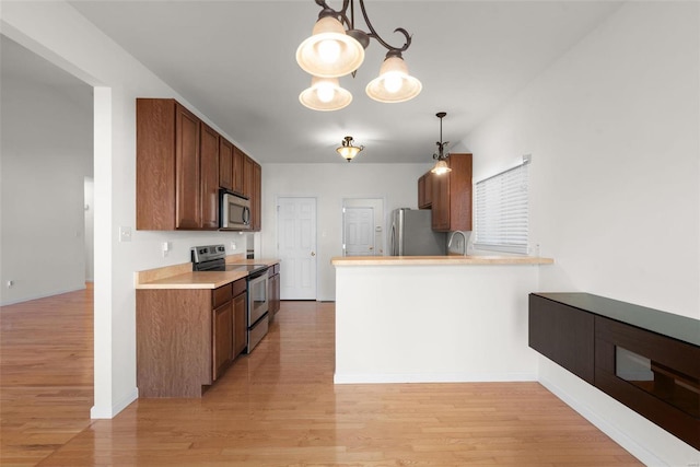 kitchen with a peninsula, hanging light fixtures, stainless steel appliances, light countertops, and light wood-type flooring