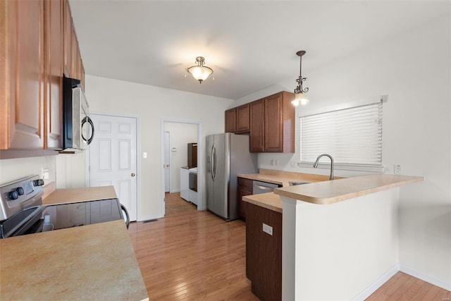 kitchen with pendant lighting, stainless steel appliances, light countertops, a sink, and a peninsula