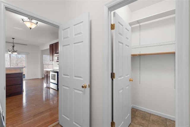 corridor featuring a notable chandelier, baseboards, and wood finished floors