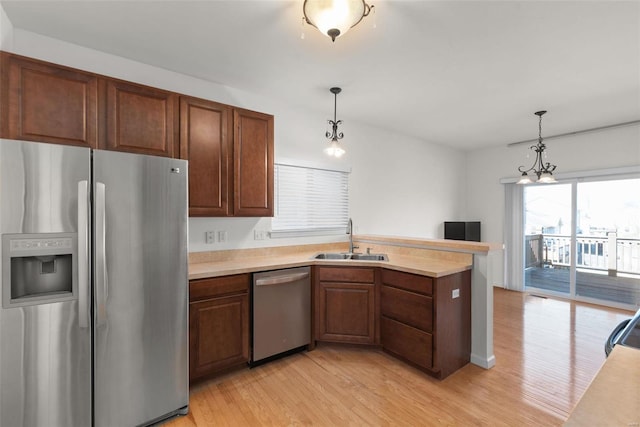 kitchen with a sink, stainless steel appliances, light countertops, and decorative light fixtures