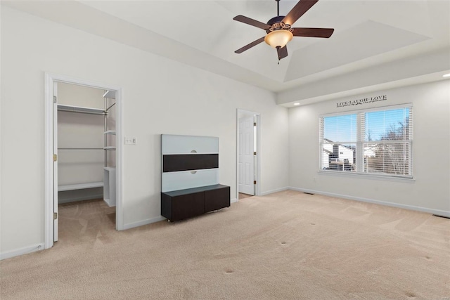 unfurnished bedroom with light carpet, a spacious closet, a tray ceiling, and baseboards