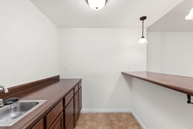 interior space featuring dark countertops, a sink, hanging light fixtures, and baseboards