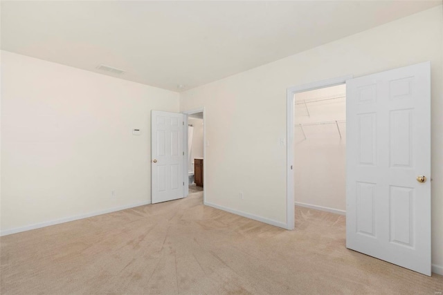 unfurnished bedroom featuring baseboards, a spacious closet, a closet, and light colored carpet