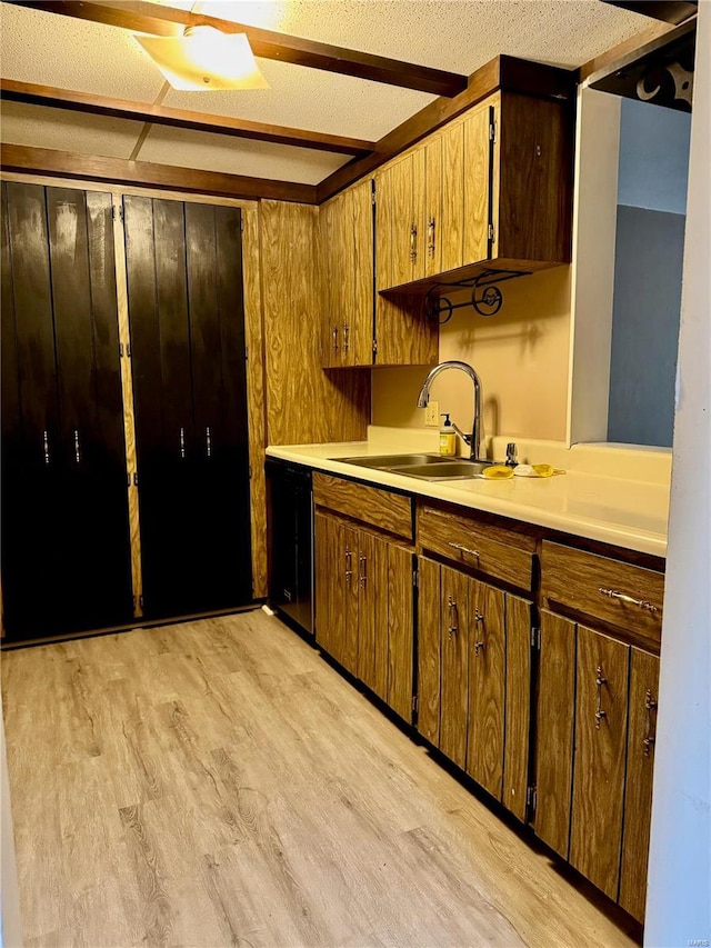 kitchen with sink, light hardwood / wood-style flooring, dishwasher, a textured ceiling, and wood walls