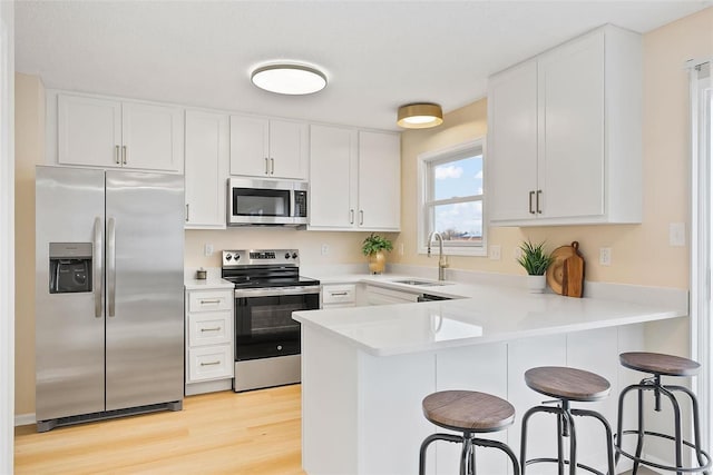 kitchen featuring a breakfast bar, sink, light hardwood / wood-style flooring, appliances with stainless steel finishes, and white cabinets