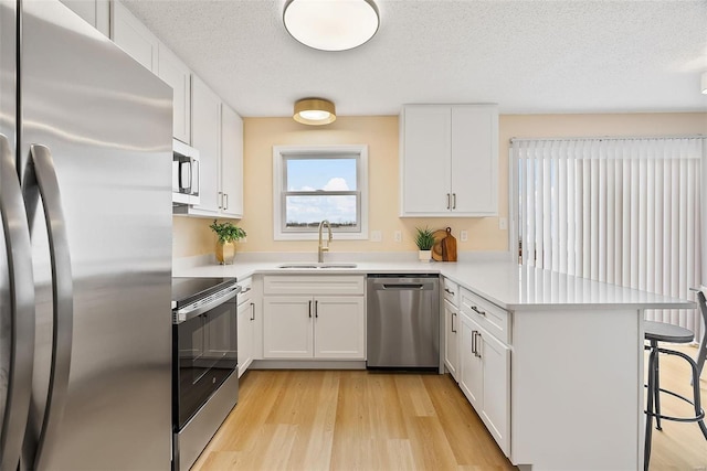 kitchen with a kitchen bar, sink, appliances with stainless steel finishes, kitchen peninsula, and white cabinets