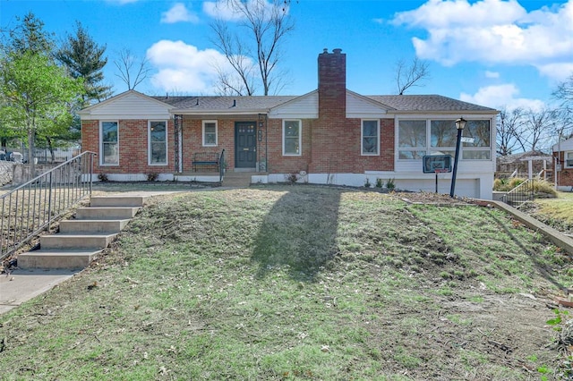 single story home featuring brick siding, a sunroom, a chimney, an attached garage, and a front yard