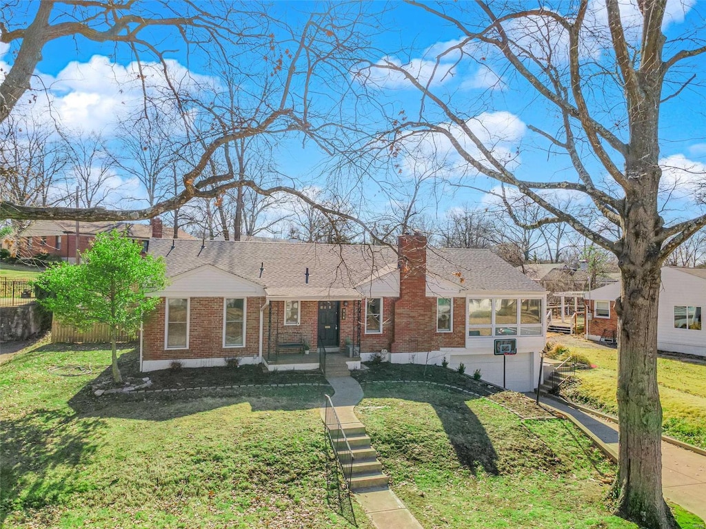 view of front of property featuring brick siding, a chimney, an attached garage, a sunroom, and a front lawn