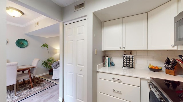 kitchen with ornamental molding, light wood-type flooring, white cabinets, and backsplash