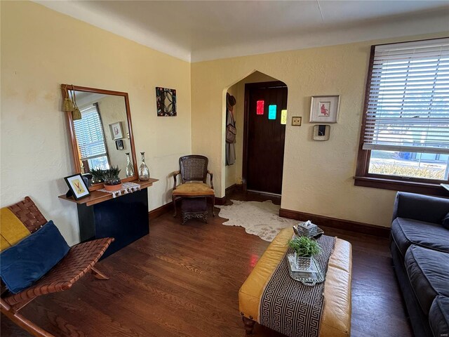 living room with arched walkways, a textured wall, baseboards, and wood finished floors