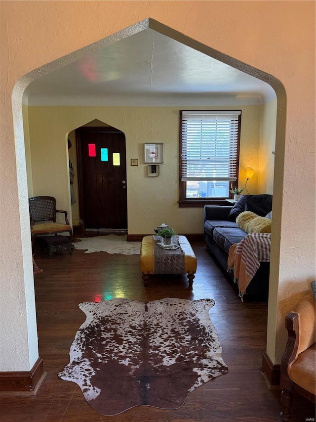 living room with arched walkways, baseboards, a textured wall, and wood finished floors