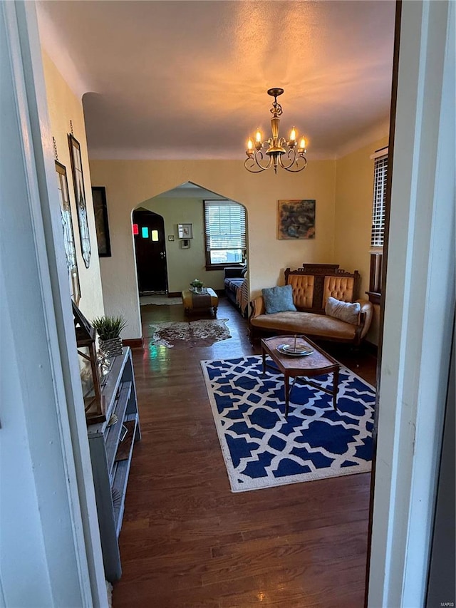 living room featuring arched walkways, a chandelier, and wood finished floors