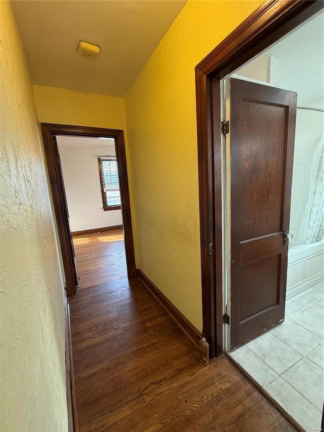 hall with a textured wall, baseboards, and wood finished floors