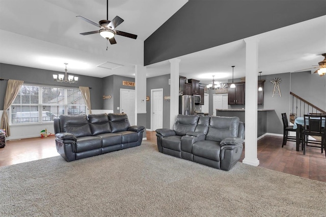 living room featuring high vaulted ceiling, ceiling fan with notable chandelier, decorative columns, and dark colored carpet