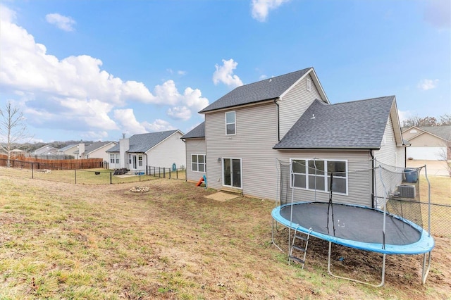 rear view of property featuring a trampoline and a lawn