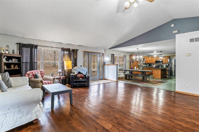 living room featuring ceiling fan with notable chandelier, light hardwood / wood-style flooring, a textured ceiling, and vaulted ceiling