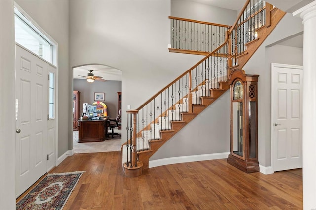 entrance foyer with hardwood / wood-style floors, a towering ceiling, ceiling fan, and ornate columns