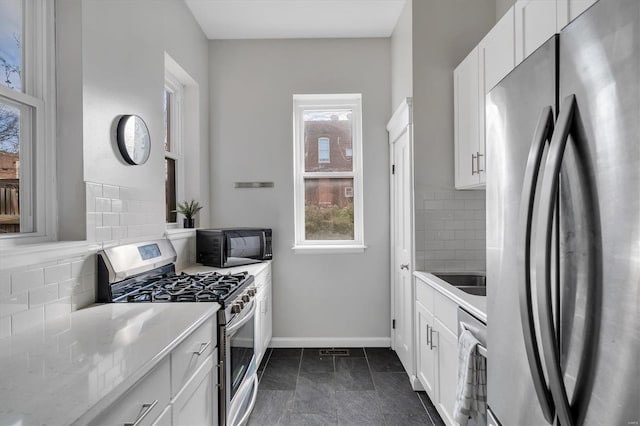 kitchen featuring stainless steel appliances, light countertops, decorative backsplash, white cabinets, and baseboards