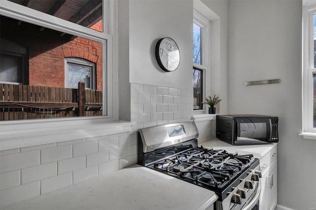 kitchen with a wealth of natural light, stainless steel range with gas cooktop, black microwave, and white cabinets