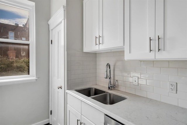 kitchen with white cabinetry, a sink, decorative backsplash, and light stone countertops