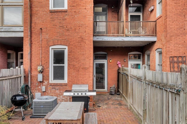 exterior space featuring central AC unit, a patio, a balcony, fence, and brick siding