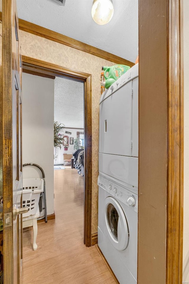 laundry area featuring stacked washer / dryer, ornamental molding, light wood-type flooring, and a textured ceiling