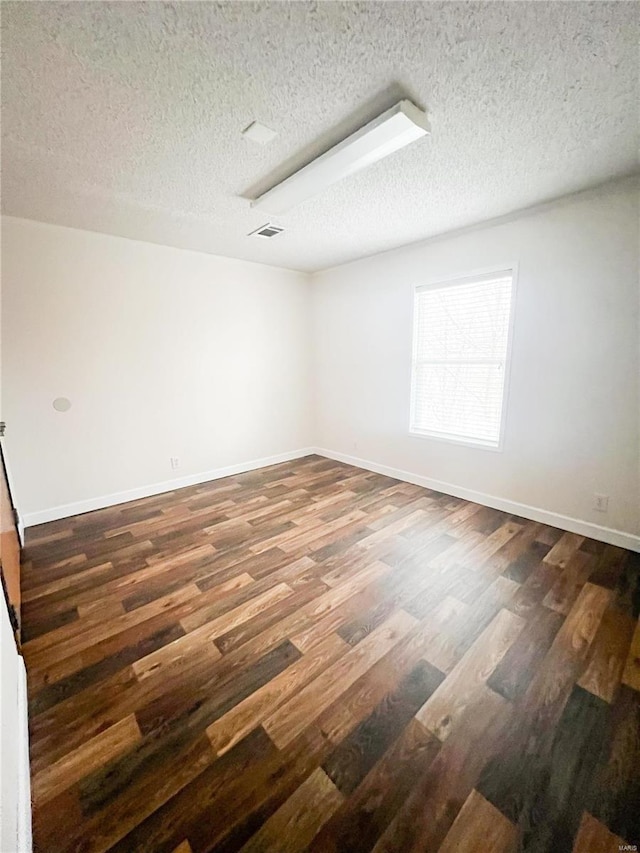 empty room with dark hardwood / wood-style floors and a textured ceiling