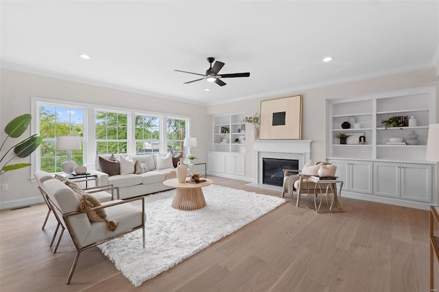 living room with crown molding, built in features, ceiling fan, a high end fireplace, and light hardwood / wood-style floors