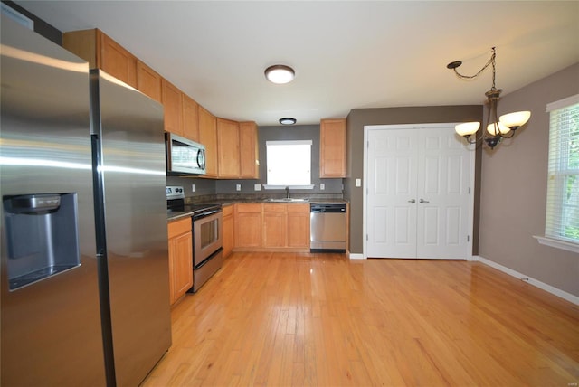 kitchen with sink, decorative light fixtures, appliances with stainless steel finishes, a notable chandelier, and light hardwood / wood-style floors