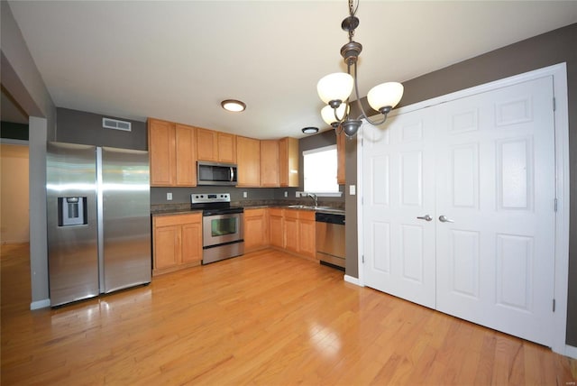 kitchen featuring appliances with stainless steel finishes, decorative light fixtures, sink, a chandelier, and light hardwood / wood-style flooring