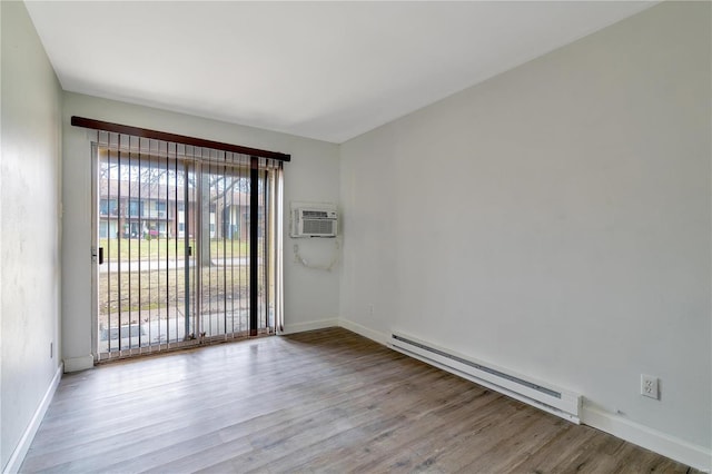 spare room featuring baseboard heating, light hardwood / wood-style floors, and an AC wall unit