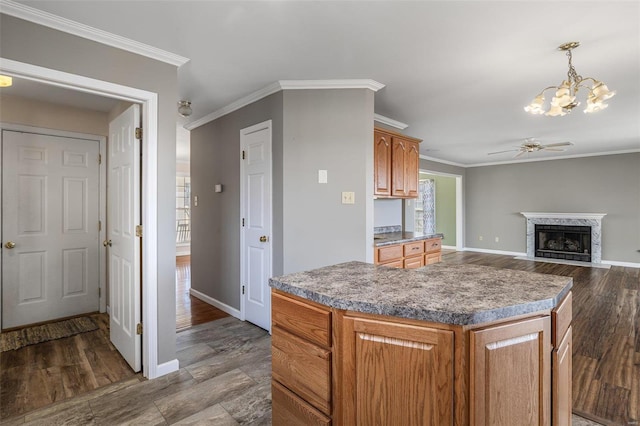 kitchen featuring ceiling fan with notable chandelier, a fireplace, decorative light fixtures, a center island, and crown molding