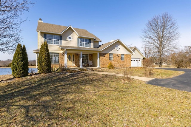 view of front facade with a garage, a water view, covered porch, and a front lawn