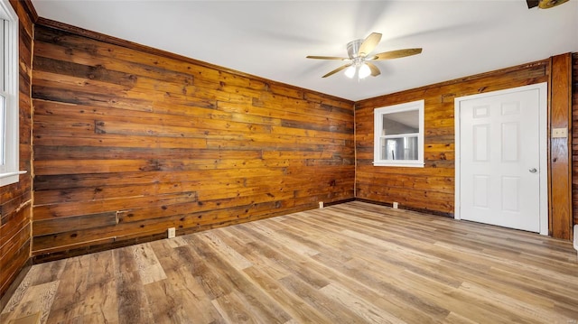 empty room with wood walls, ceiling fan, and light hardwood / wood-style flooring