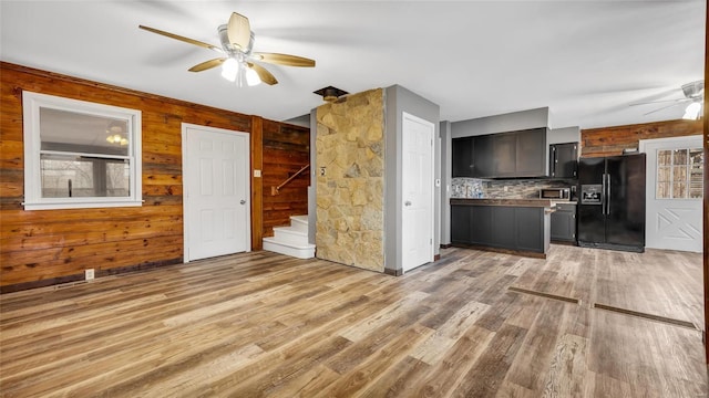 kitchen with wood walls, tasteful backsplash, light hardwood / wood-style floors, ceiling fan, and black refrigerator with ice dispenser