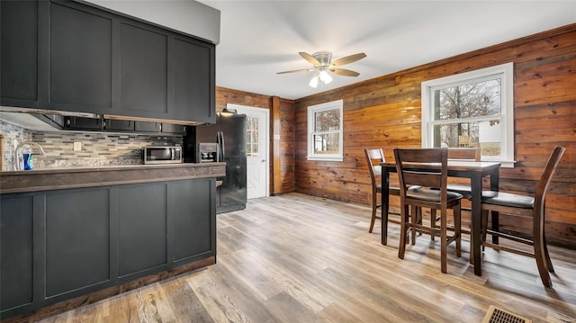 kitchen with black fridge with ice dispenser, wood walls, light hardwood / wood-style flooring, ceiling fan, and decorative backsplash